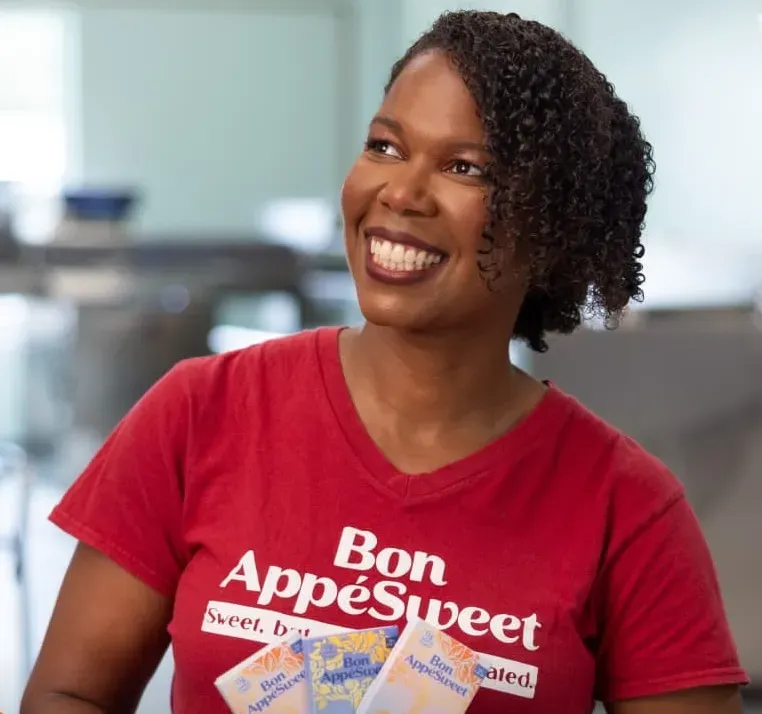 Thereasa Black smiling in a red Bon AppéSweet T-shirt with chocolate bars in front of her.